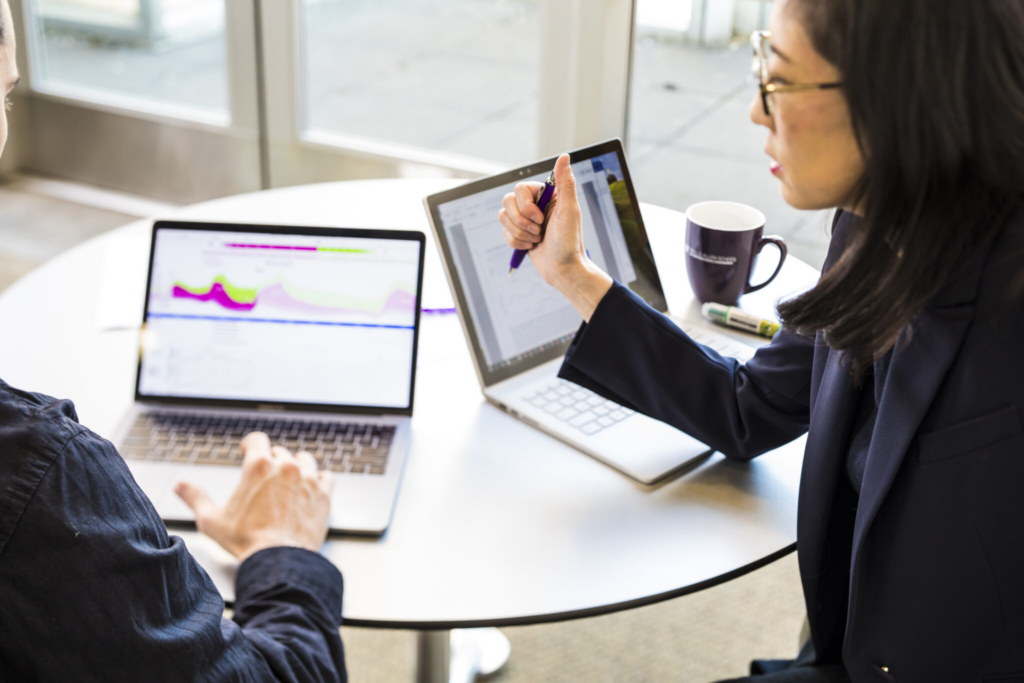 two people looking at charts on laptops